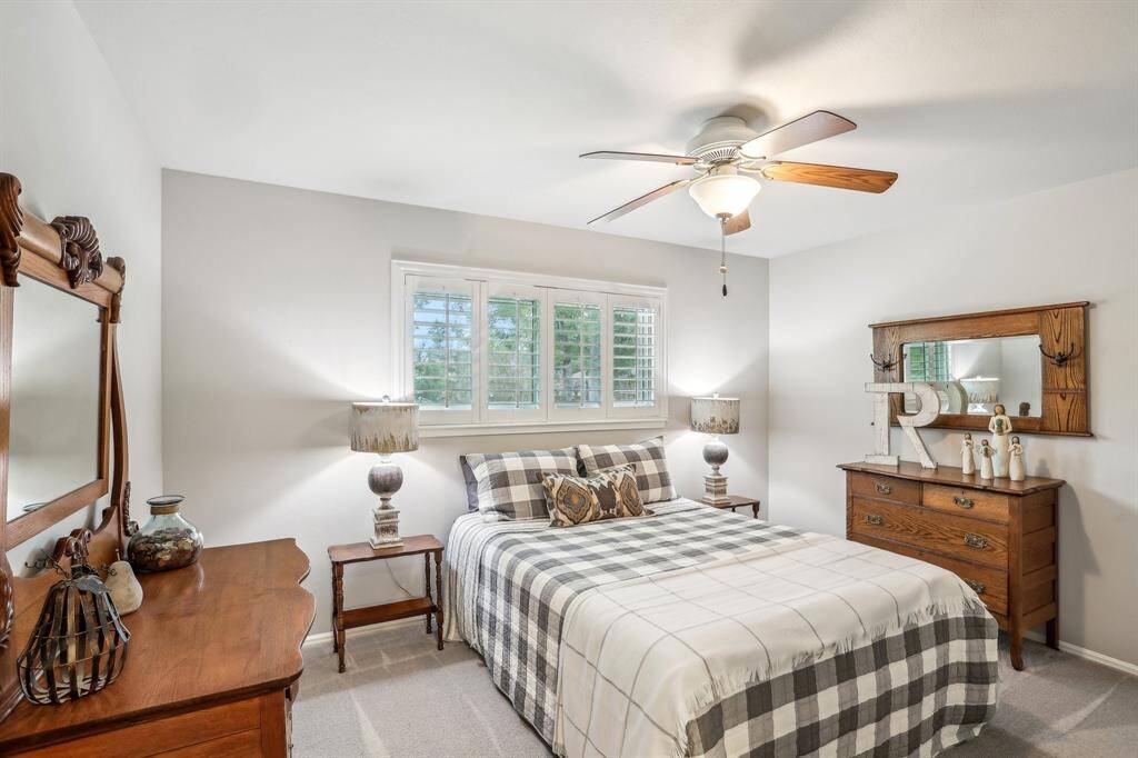 This cozy bedroom features ample space and a ceiling fan. Natural light streams in through a window with plantation shutters, creating a bright and inviting atmosphere.