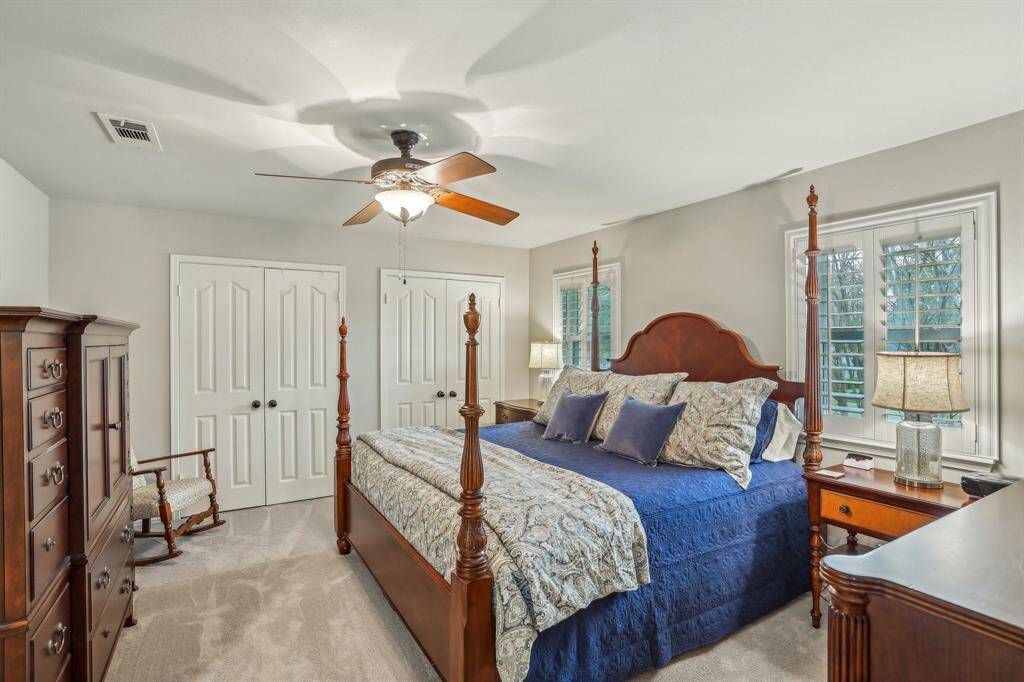 This spacious bedroom features soft carpeting and ample natural light from two large windows with plantation shutters.