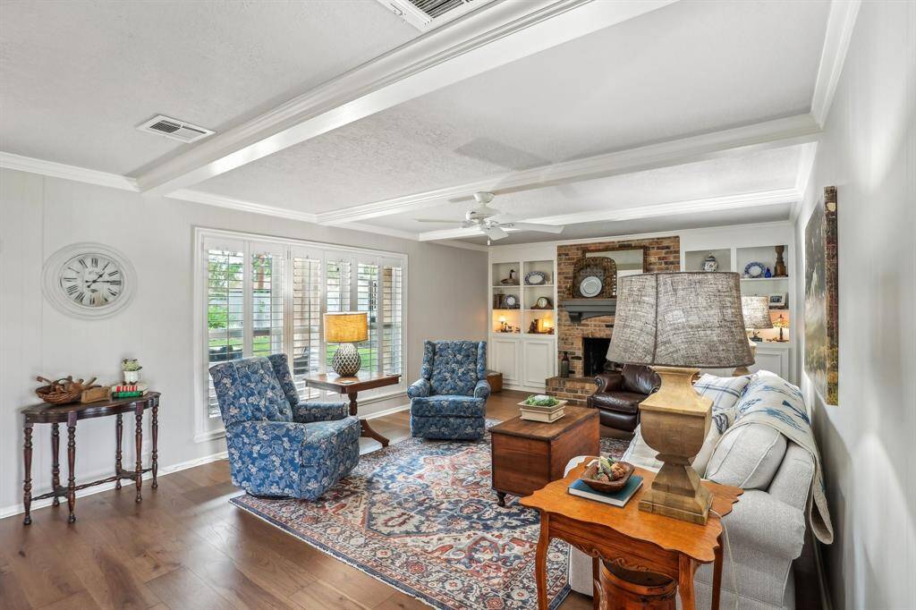 This cozy living room features a classic design with a brick fireplace, built-in shelves, and large windows for natural light. The space provides for comfortable seating, a decorative rug, and elegant wood flooring, creating a warm and inviting atmosphere.