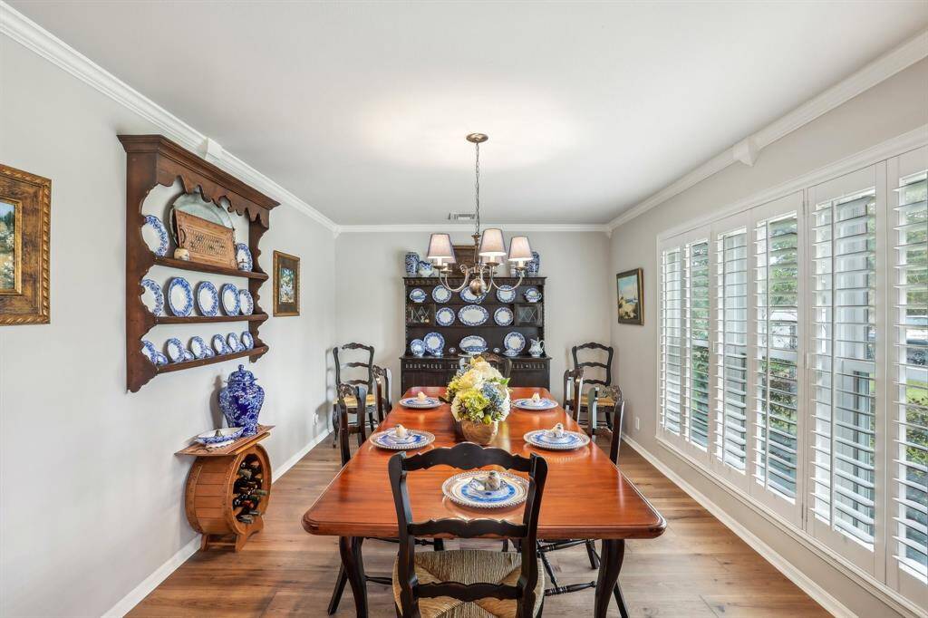 This dining room features elegant wood flooring, plenty of room for a large table, and  ample natural light from the wide windows with shutters.