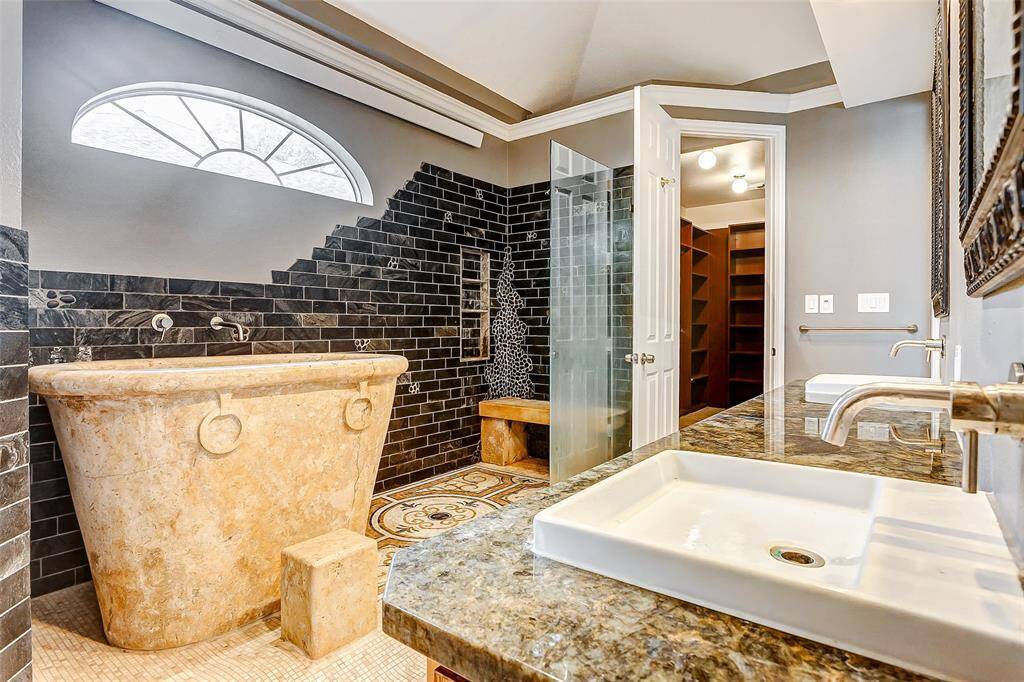 Indulge in spa-like luxury with a custom soaking tub, sleek black tiled walls, dual sinks, and a walk-in shower.