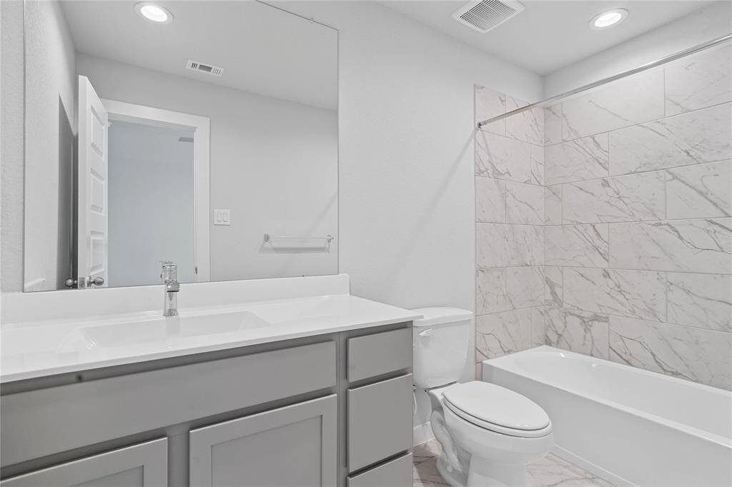 Secondary bath features tile flooring, bath/shower combo with tile surround, stained wood cabinets, beautiful light countertops, mirror, sleek fixtures and modern finishes.