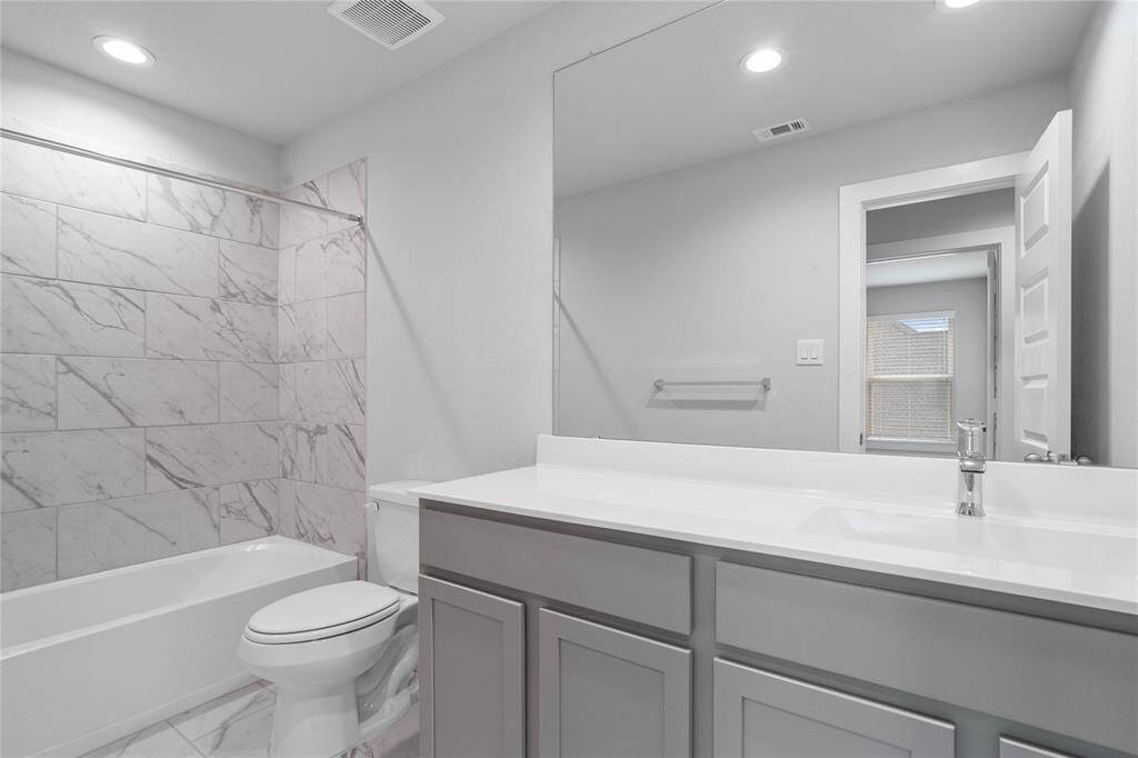 Secondary bath features tile flooring, bath/shower combo with tile surround, stained wood cabinets, beautiful light countertops, mirror, sleek fixtures and modern finishes.