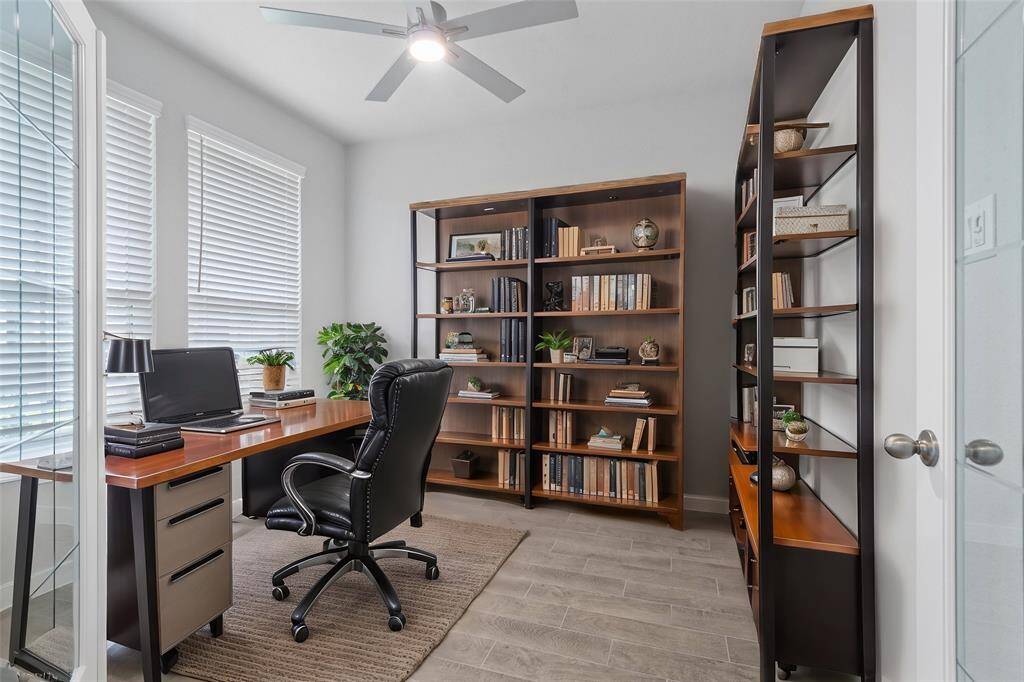 Quietly nestled in front of the home is the handsome home office. Featuring French doors, wood look tile flooring, high ceilings, ceiling fan, large windows with privacy blinds and custom paint.