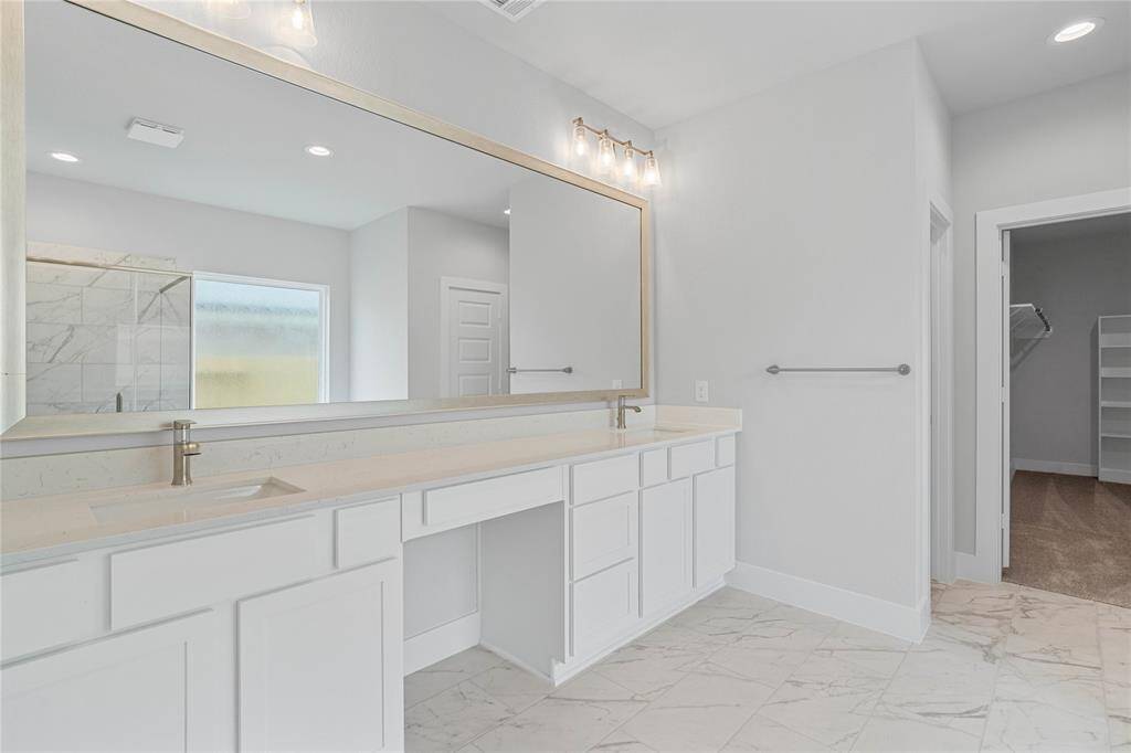 This primary bathroom is definitely move-in ready! Featuring stained cabinets with light countertops, dual vanity sinks, large framed mirror, spacious walk-in closet with shelving, high ceilings, custom paint, and sleek modern finishes.