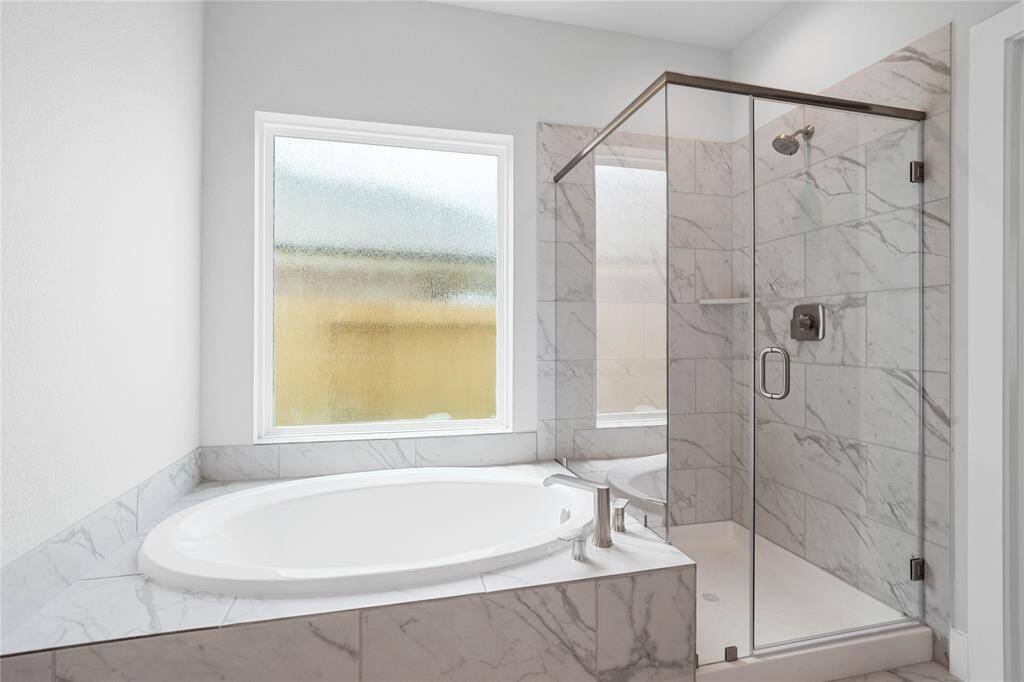 This additional view of the primary bath showcases a walk-in shower with tile surround, separate garden tub perfect for soaking after a long day, and a large rain glass window.
