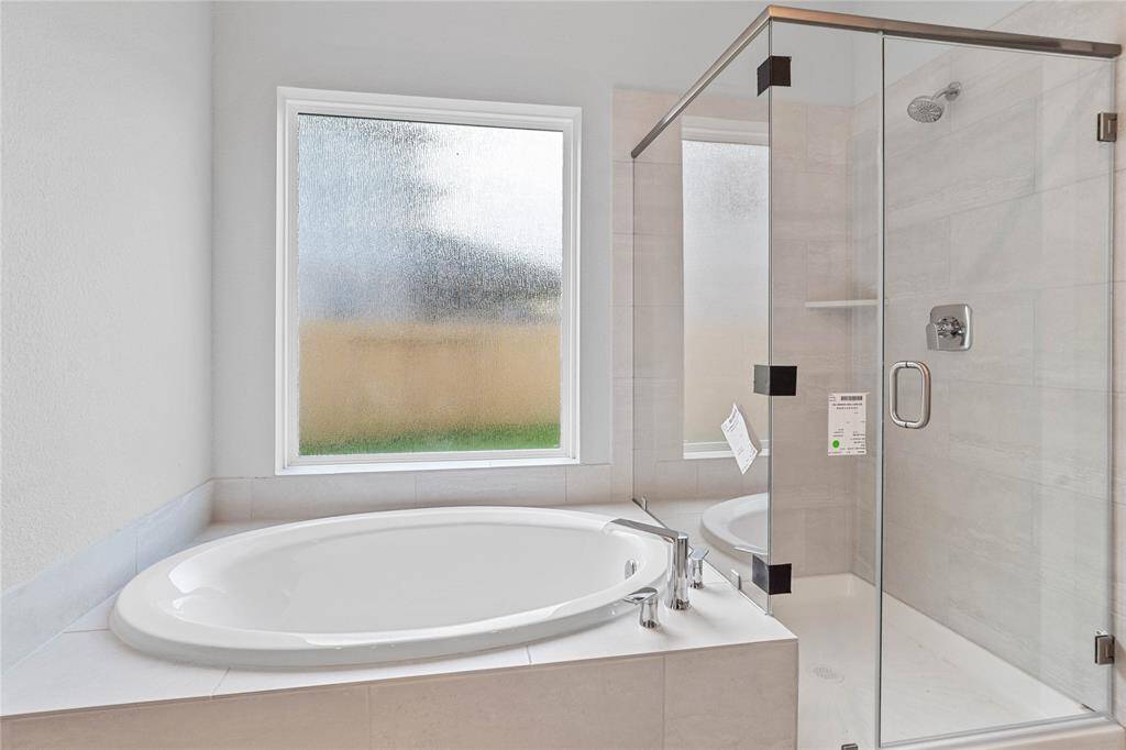 Additional view of this beautiful primary bathroom features a dark framed walk-in shower with tile surround, separate garden tub for soaking after a long day with custom tile detailing, high ceilings, custom paint, and a large rain glass window allowing in the natural lighting.
