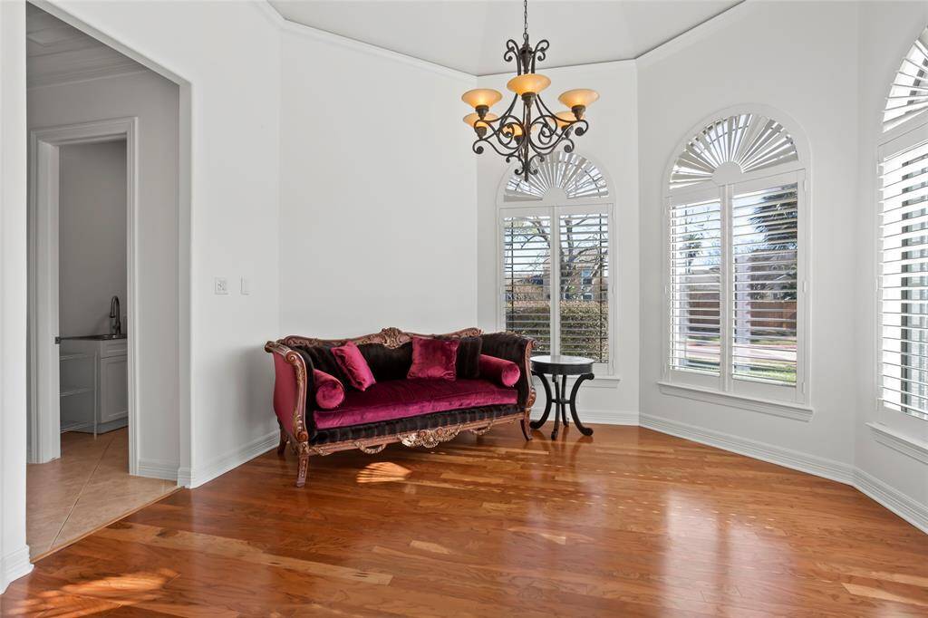 This bright room features elegant hardwood floors, large arched windows with shutters, and a stylish chandelier. The space is enhanced by an ornate burgundy sofa, creating a welcoming and sophisticated atmosphere. Perfect for a sitting area, music room or second home office.