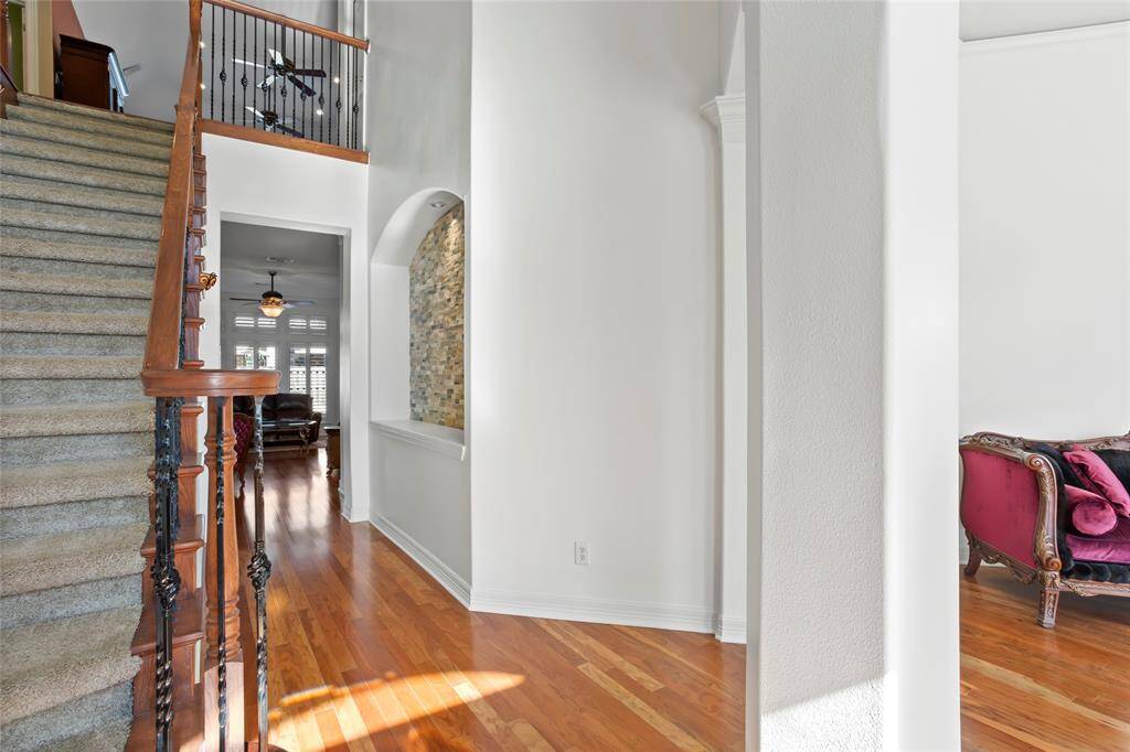 This two story has a bright entryway with hardwood floors, a carpeted staircase with wood and wrought iron railing, and an arched alcove with accent stonework. The space opens into a living area with large bay windows overlooking the pool and spa.