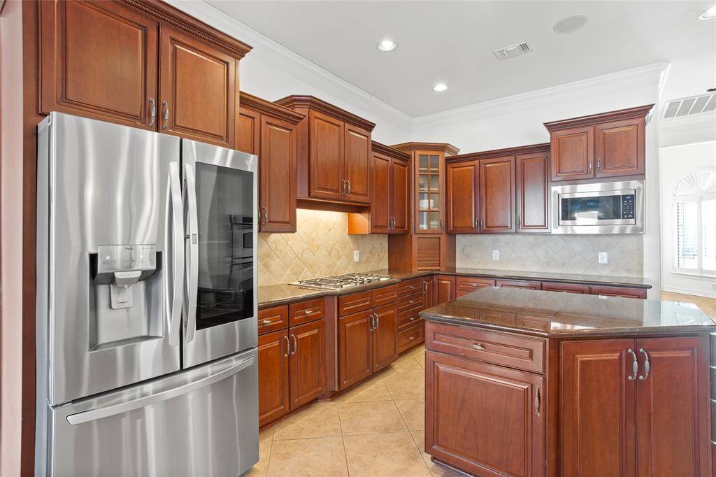 This kitchen features elegant wood cabinetry, granite countertops, a central island, and stainless steel appliances (new LG Refrigerator and LG Microwave). It’s spacious and well-lit, offering a modern and functional cooking space.