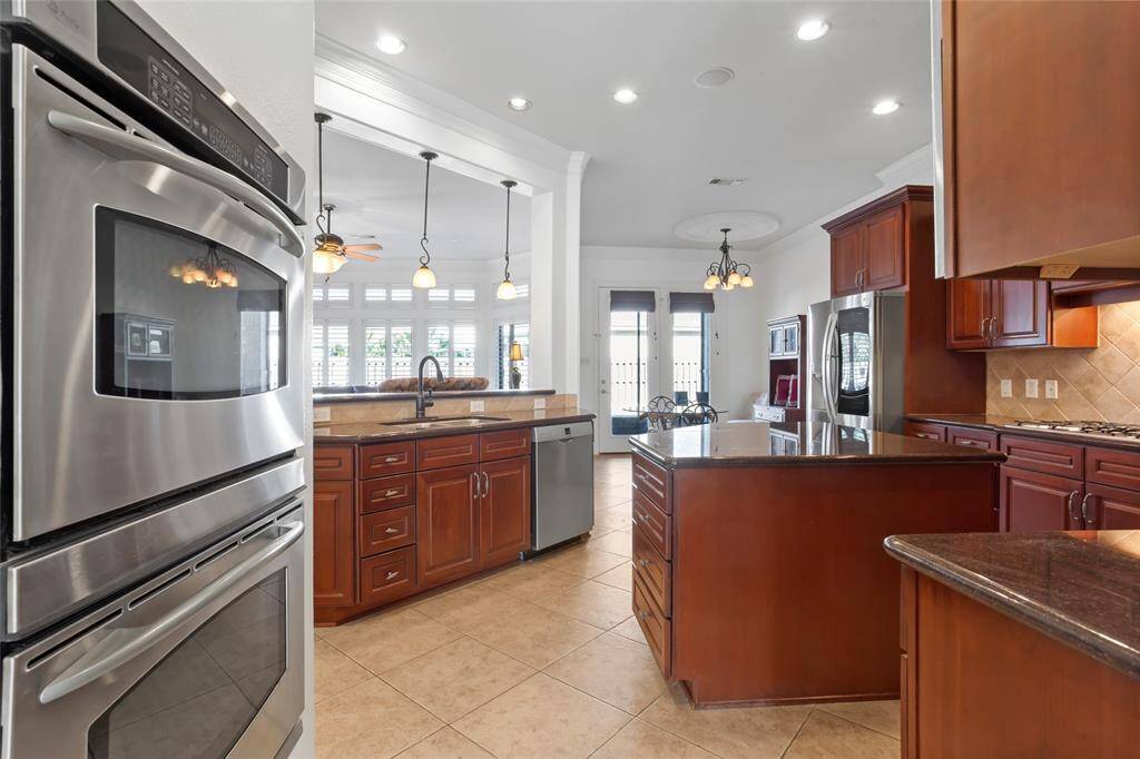 This spacious kitchen features stainless steel appliances, rich wooden cabinetry, and a large central island. The open layout connects to a bright dining area with large windows and elegant lighting, offering a welcoming and modern space.