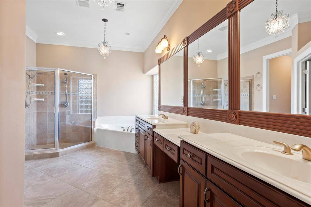 This spacious primary bathroom features a double vanity with elegant wooden cabinets, large mirrors, and stylish lighting. It includes a glass-enclosed shower and a separate extra large soaking tub, all set against neutral-toned tiles for a luxurious feel.