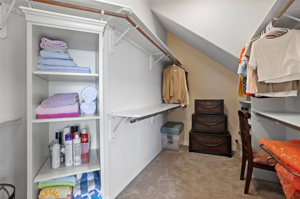 The primary bathroom has a spacious walk-in closet with ample shelving and hanging space. It features carpeted flooring and additional storage with stacked drawers and bins.