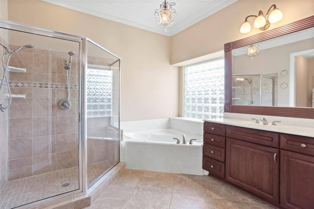 This bathroom features a spacious glass-enclosed shower, a large jetted soaking tub, and a double-sink vanity with elegant wooden cabinetry. Natural light streams through a privacy glass window, enhancing the bright, welcoming atmosphere.