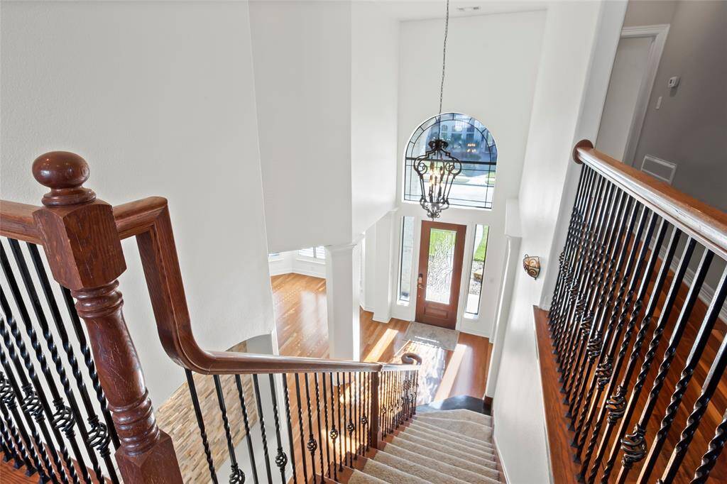 A bright and elegant entryway with a grand staircase. The space features a high ceiling, a large arched window above the front door, and a stylish chandelier, creating an inviting atmosphere. The staircase has wood and wrought iron railings, adding a touch of sophistication.