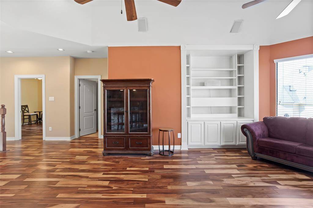 This spacious living or entertainment area features rich brazilian hardwood floors, a built-in white shelving. The room is accented with warm colors and neutral walls, creating an inviting atmosphere. Natural light streams in through large windows, enhancing the open feel.