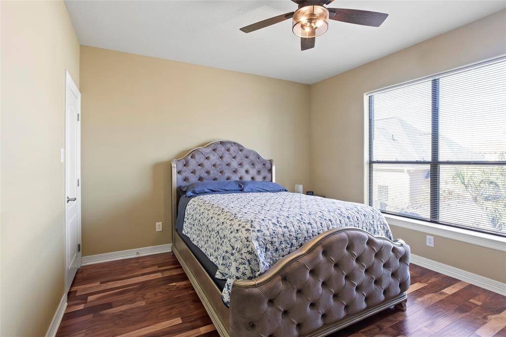Cozy bedroom with brazilian hardwood floors, large window for natural light. Neutral wall color complements the ceiling fan for a comfortable atmosphere.