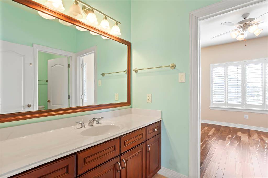 A bright, well-lit jack and jill style bathroom with a large mirror, double vanity, and elegant wooden cabinetry. Combination shower and bathtub and ample storage space.