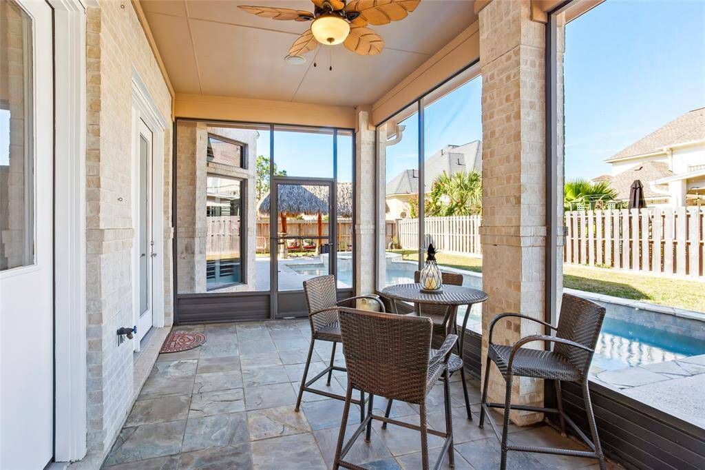 This cozy sunroom features a tiled floor, a ceiling fan, and large windows offering a view of the backyard and pool area. It's furnished with a wicker dining set, creating a perfect space for relaxation and entertaining.