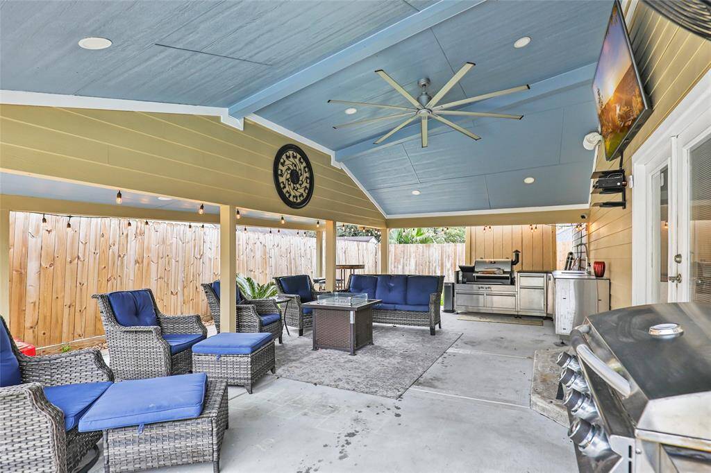 Huge covered patio with outdoor kitchen, ceiling fan, advanced lighting, and shades.