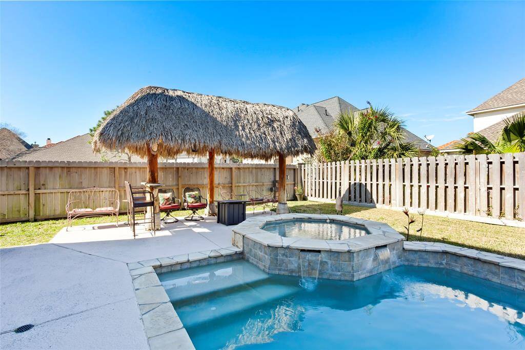 This backyard features a refreshing pool with an attached spa and a charming thatched-roof tiki hut, perfect for outdoor relaxation and entertaining. The space is newly fenced for privacy, offering a tropical retreat in your own home.