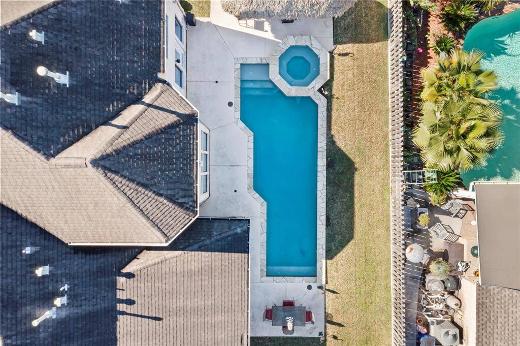 This aerial photo showcases a beautiful backyard with a rectangular swimming pool and attached spa, surrounded by a spacious patio area. The property features a well-maintained lawn and is newly fenced for privacy, with some lush greenery adding to the appeal.