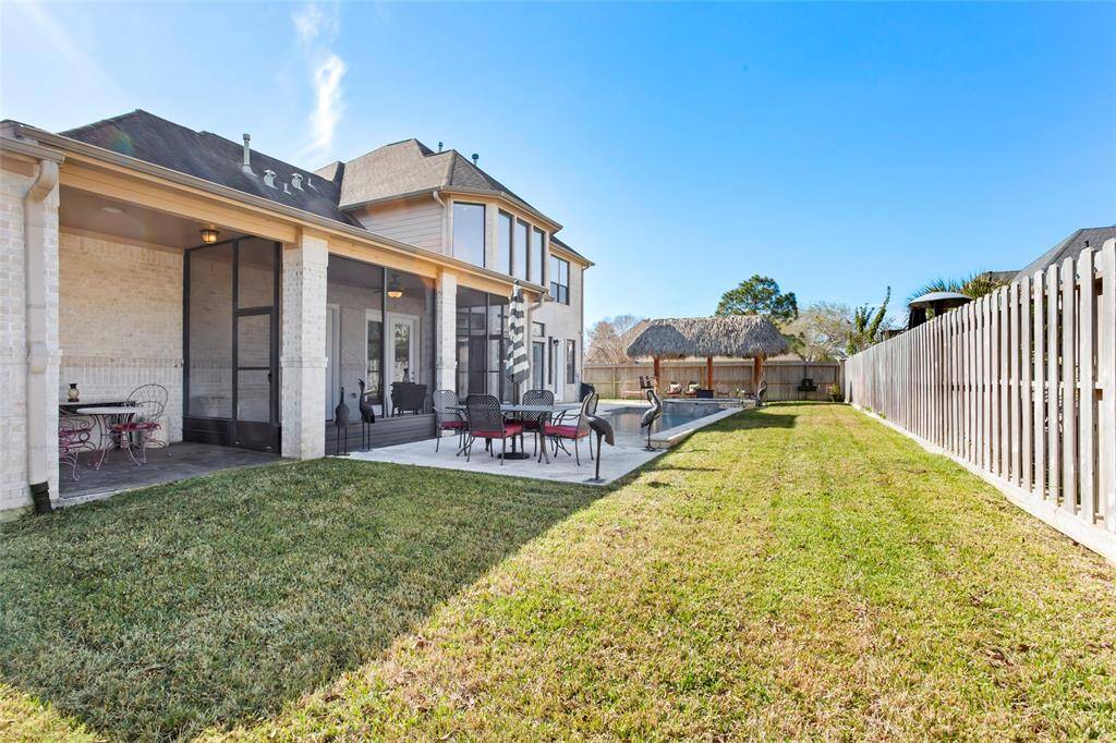 This photo showcases a spacious backyard with a screened patio, outdoor seating area, and a pool. The well-maintained lawn and new privacy fence create a serene outdoor space, ideal for relaxation and entertaining.