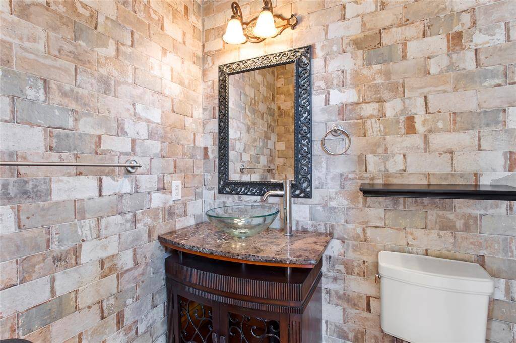 This is a stylish half bath on the first level with rustic brick walls, featuring a decorative mirror above a modern glass vessel sink on a marble countertop.