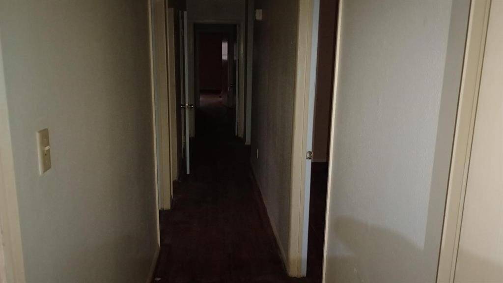 This photo shows a narrow, dimly lit hallway with multiple doors leading to different rooms. The walls are plain, and the floor appears to be carpeted.