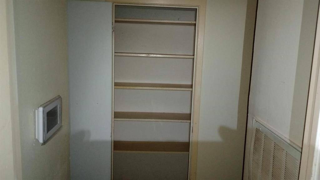 This photo shows a small storage area or closet with multiple shelves, ideal for organizing household items. There is a thermostat on the wall, suggesting proximity to a living area. The space is narrow but functional.