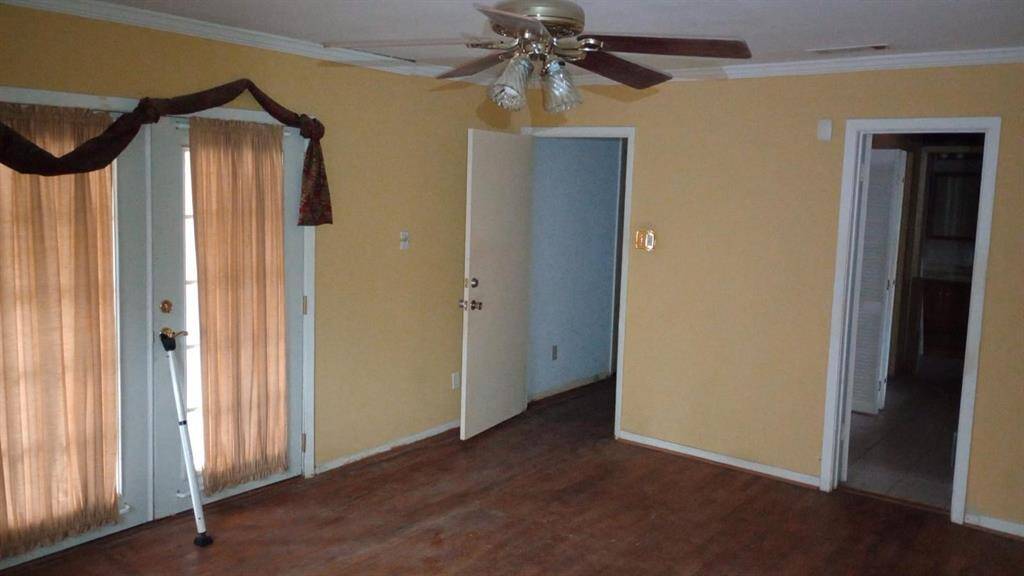 This room features warm yellow walls and hardwood flooring, with natural light filtering through sheer curtains on French doors. It includes a ceiling fan and provides access to adjacent rooms and a hallway.