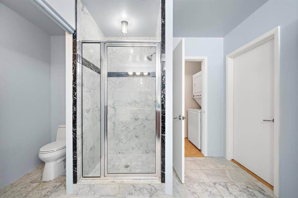 A walk-in shower with marble tile. WC has a fold up door. The door on the right leads out into the hallway.