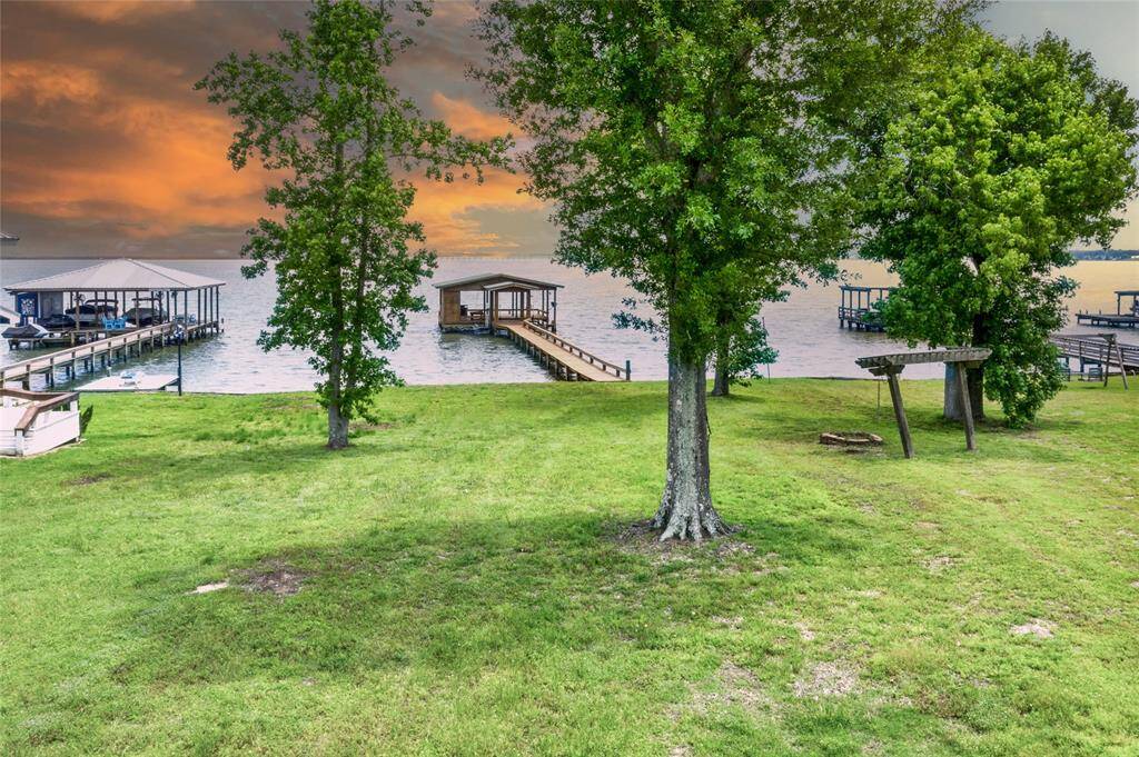 Lakefront property on Lake Livingston with lush green grass and mature trees. It includes a beautiful wooden dock with a large boathouse extending into the lake, perfect for boating or fishing and entertaining. Enjoy the inviting ambiance and sunsets all ideal for peaceful lakeside living.