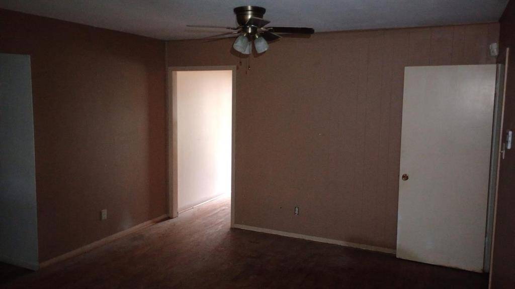 This room features neutral walls and wood flooring, with a ceiling fan providing air circulation. It has a door leading to another space, offering potential for customization and personal touches.