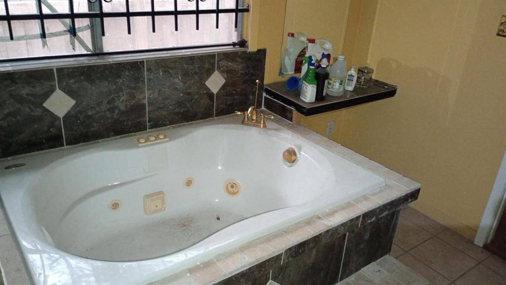 This bathroom features a spacious jacuzzi tub with marble tile accents and a small shelf for toiletries. A window with security bars provides natural light.