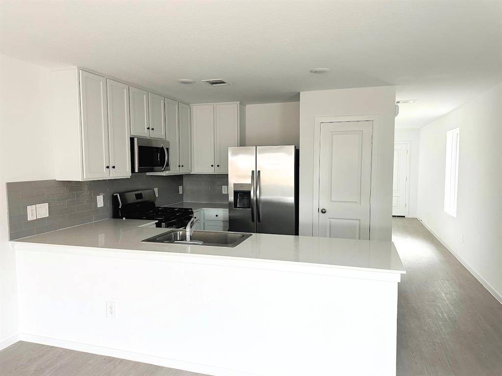 The kitchen has stainless steel appliances, tile back splash and a pantry