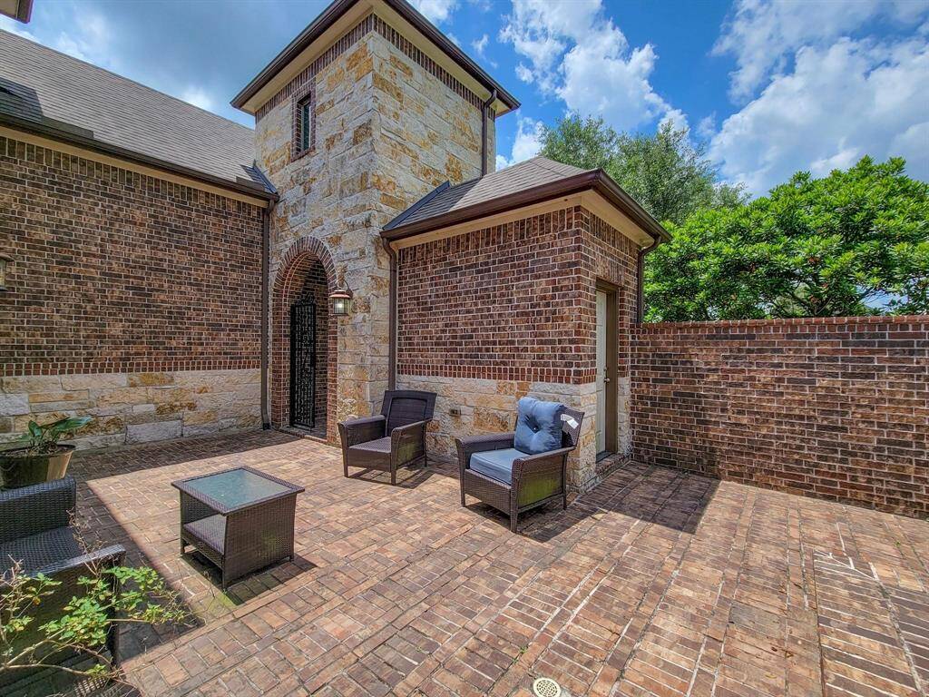Charming two-story brick home with a spacious driveway leading to a two-car garage. The front yard is well-maintained with lush grass, landscaping, and a mature tree, all set against a backdrop of a blue sky with clouds.
