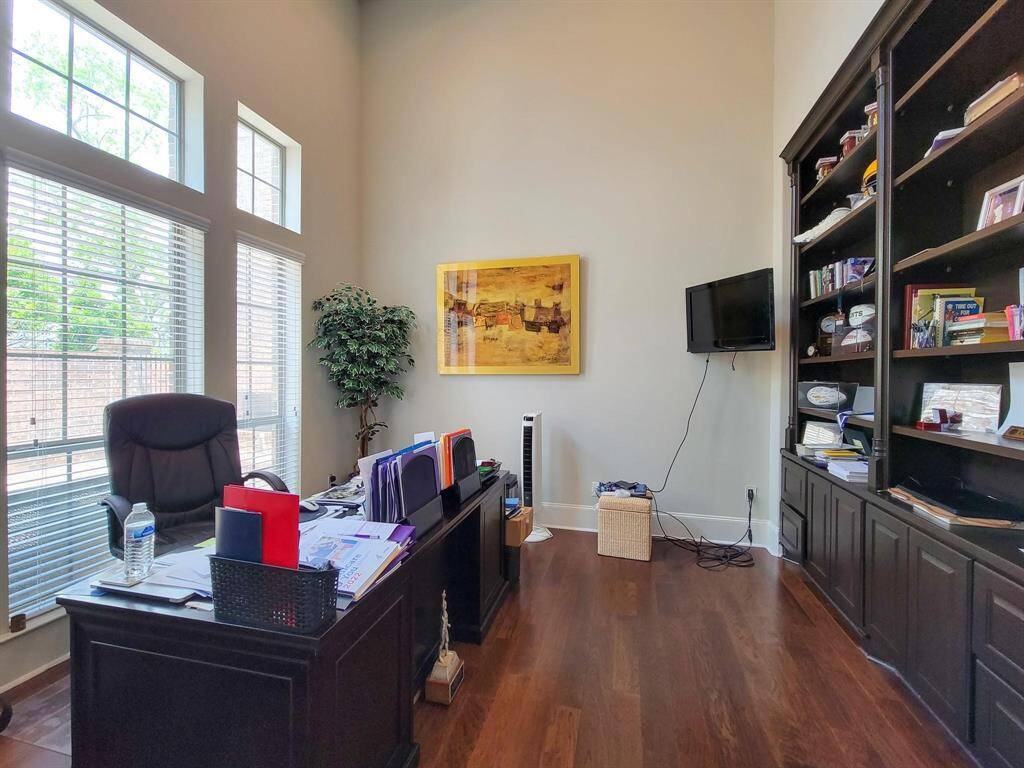 Home office with high ceilings, large windows, and wood flooring. It features a spacious desk, a wall-mounted TV, and built-in bookshelves, creating a functional and inviting workspace.