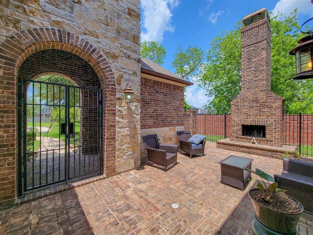 This outdoor patio/courtyard features a charming brick fireplace, cozy seating area, and decorative gate, all surrounded by lush greenery—ideal for relaxing or entertaining.