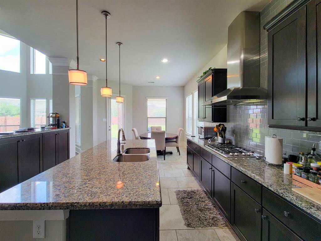 Modern kitchen with granite countertops, dark cabinetry, and stainless steel appliances. Features a large island with pendant lighting and an open dining area with abundant natural light.