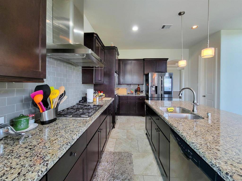 This modern kitchen features sleek dark cabinetry, granite countertops, and stainless steel appliances. The spacious layout includes a large island with a double sink and pendant lighting, perfect for cooking and entertaining.