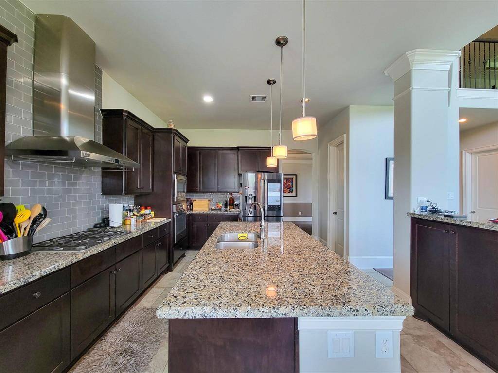 Spacious kitchen featuring dark wood cabinets, granite countertops, a large island with pendant lighting, and modern stainless steel appliances. Perfect for cooking and entertaining.