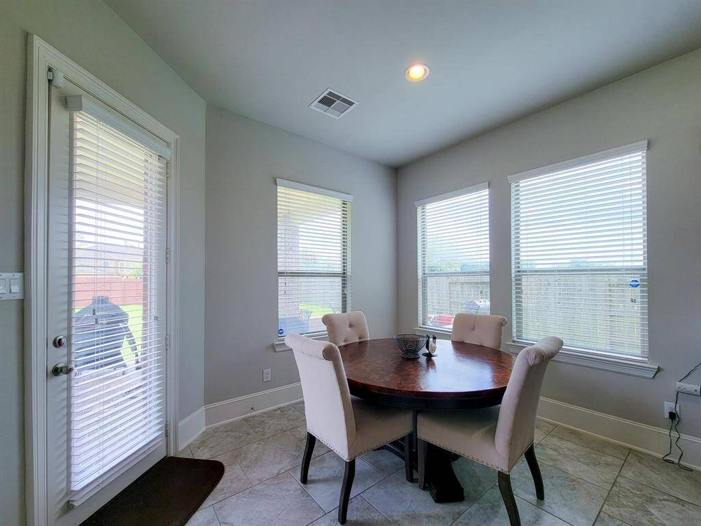 Bright dining area with large windows, offering abundant natural light. Features a round table with upholstered chairs and easy access to an outdoor patio through a glass door. Neutral tones create a welcoming atmosphere.