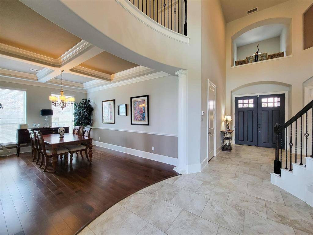 Open and elegant entryway with high ceilings, beautiful tile flooring, and a grand staircase. Adjacent is a formal dining area featuring rich wood floors, crown molding, and large windows that let in natural light. The space is bright and welcoming, ideal for entertaining.
