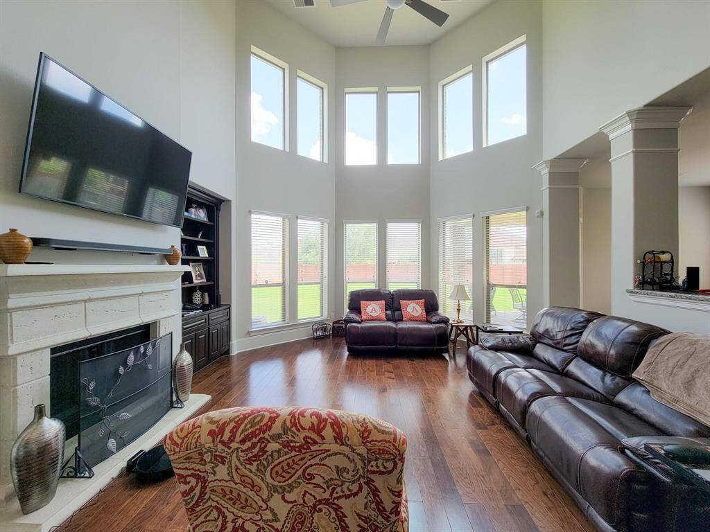This spacious living room features high ceilings and large windows, allowing plenty of natural light. It has a cozy fireplace, hardwood floors, and modern furnishings, creating an inviting atmosphere perfect for relaxation and entertainment.