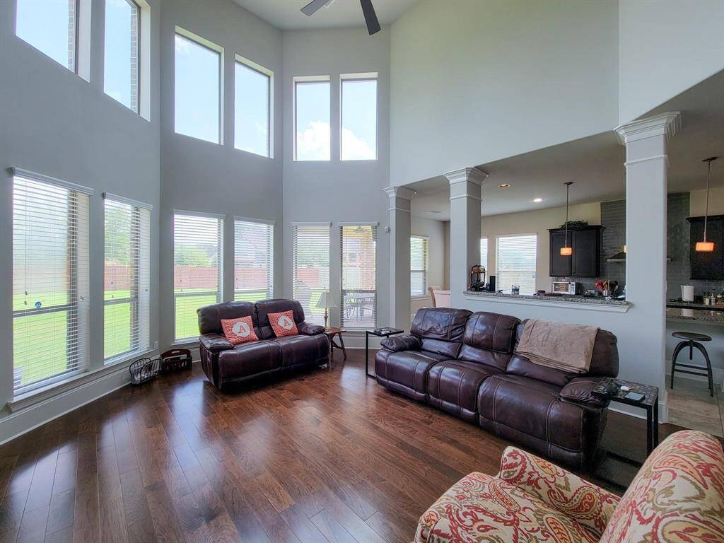 Spacious living room with high ceilings and large windows offering plenty of natural light. Features hardwood floors and an open layout that connects to the kitchen, creating a welcoming and modern atmosphere.