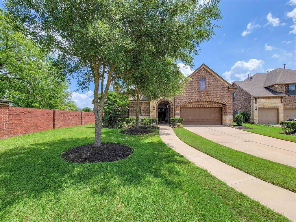 Charming brick home with a three-car garage, lush green lawn, and mature trees. Features a welcoming pathway and a spacious driveway, offering great curb appeal in a serene neighborhood.