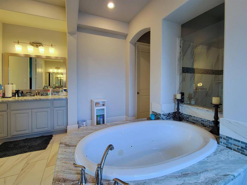 This spacious bathroom features a luxurious soaking tub, dual vanity with ample lighting, and a modern glass-enclosed shower. The elegant tile work and neutral tones create a relaxing and sophisticated atmosphere.