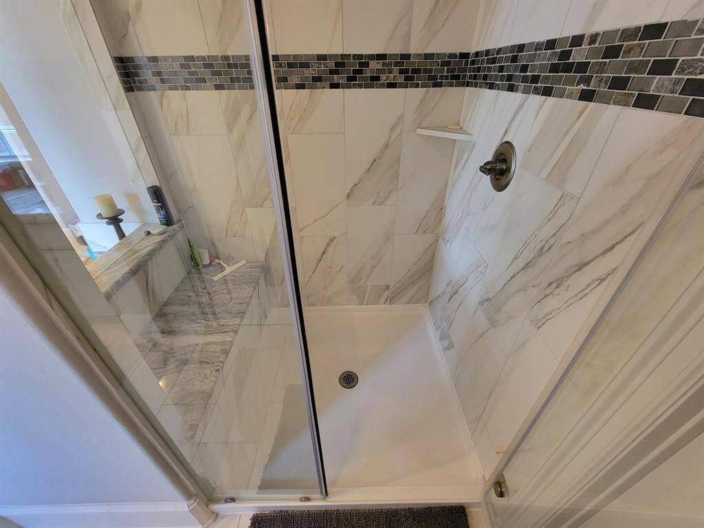 Modern shower with elegant marble-like tiles and a glass door. It features a sleek metal showerhead and a decorative mosaic tile accent strip. The design is clean and contemporary.