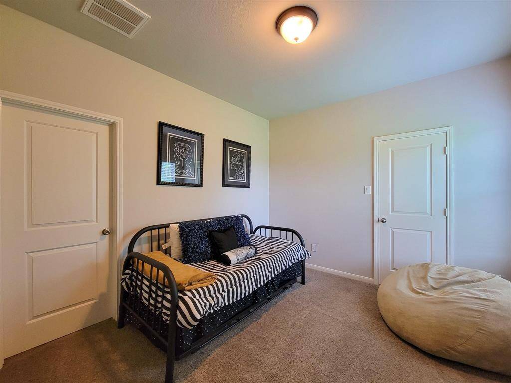 This cozy bedroom features neutral walls, carpet flooring, and a ceiling light. It includes a stylish daybed with striped bedding, two decorative wall frames, and a large bean bag, creating a welcoming and versatile space.